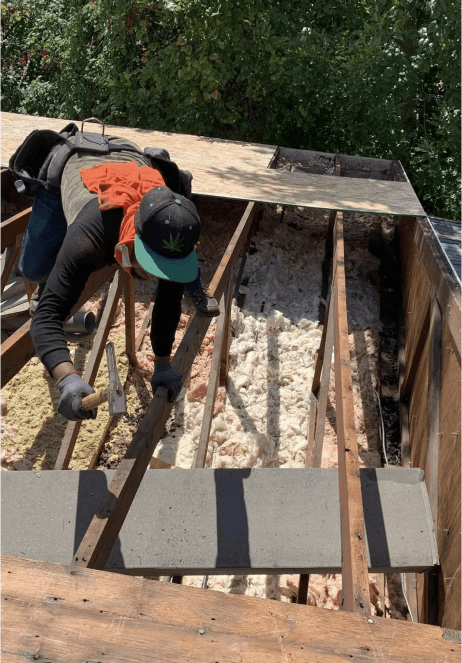 Worker rebuilding roof with hammer and nails.